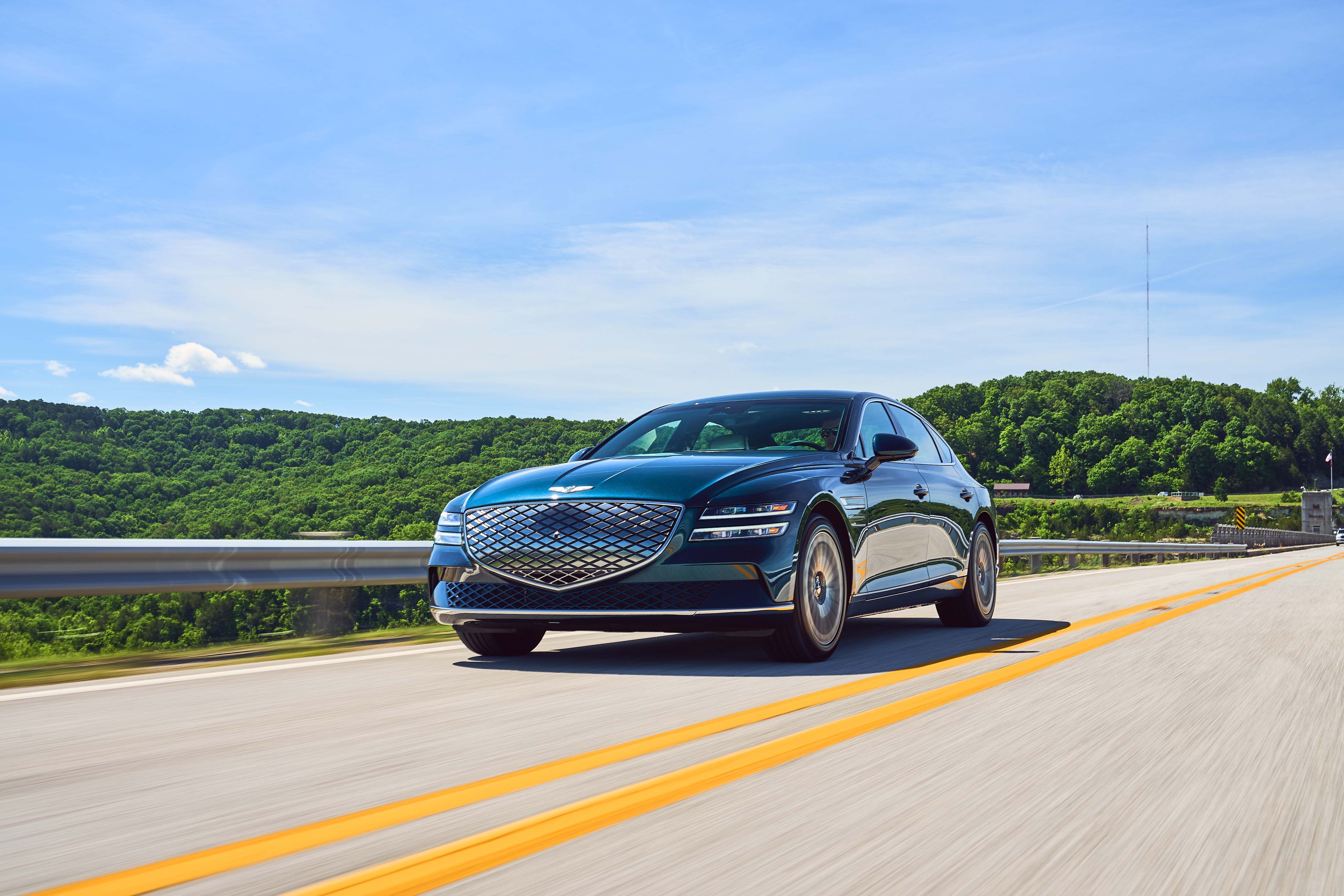 A luxury sedan driving on a scenic highway with green hills and a blue sky in the background