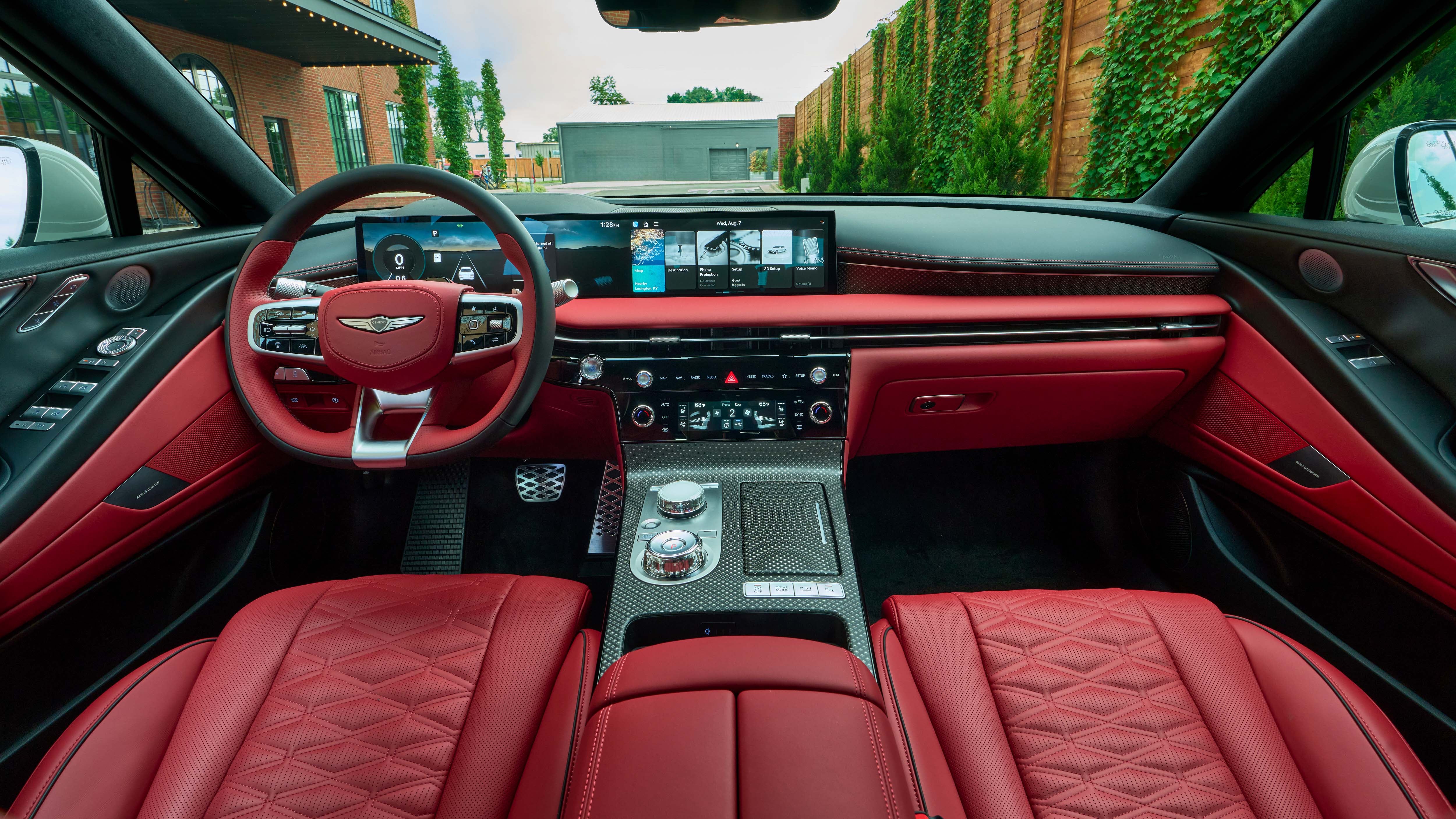 Interior view of a car with red leather seats, a dashboard with a large infotainment screen, and a steering wheel with multiple controls.