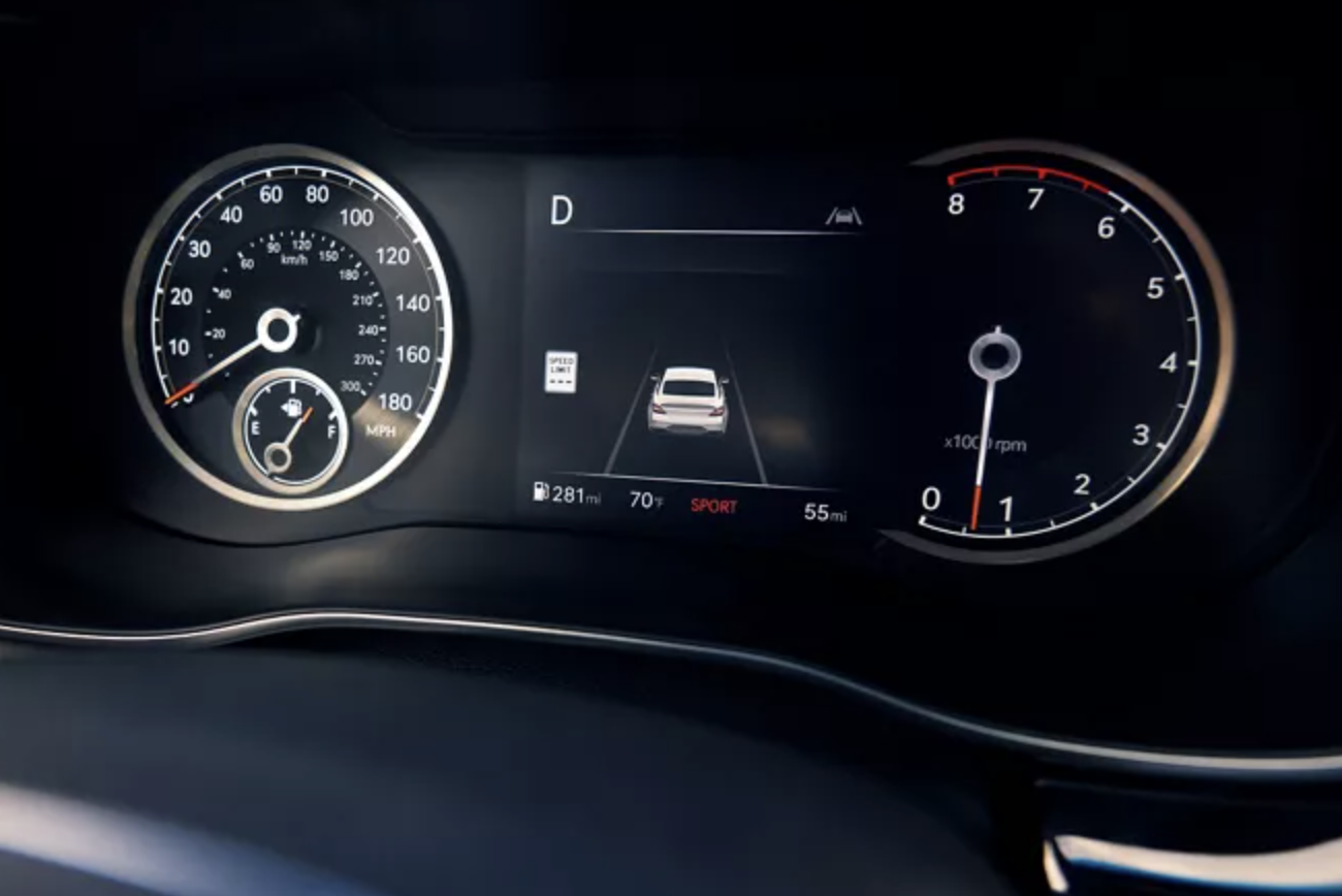 A close-up of a Genesis G70's dashboard showing the driver's perspective. The speedometer reads 70 mph, and the tachometer is at 1000 rpm. The car is in "Sport" mode.