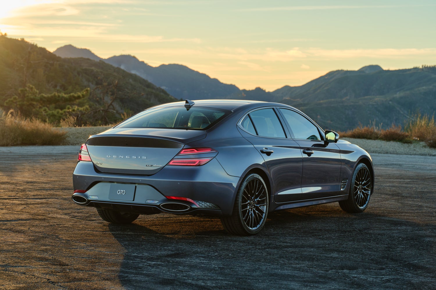 A makalu gray new G70 is parked facing away from the viewer to the right on a flat gravel lot high in the mountains in dusk lighting.