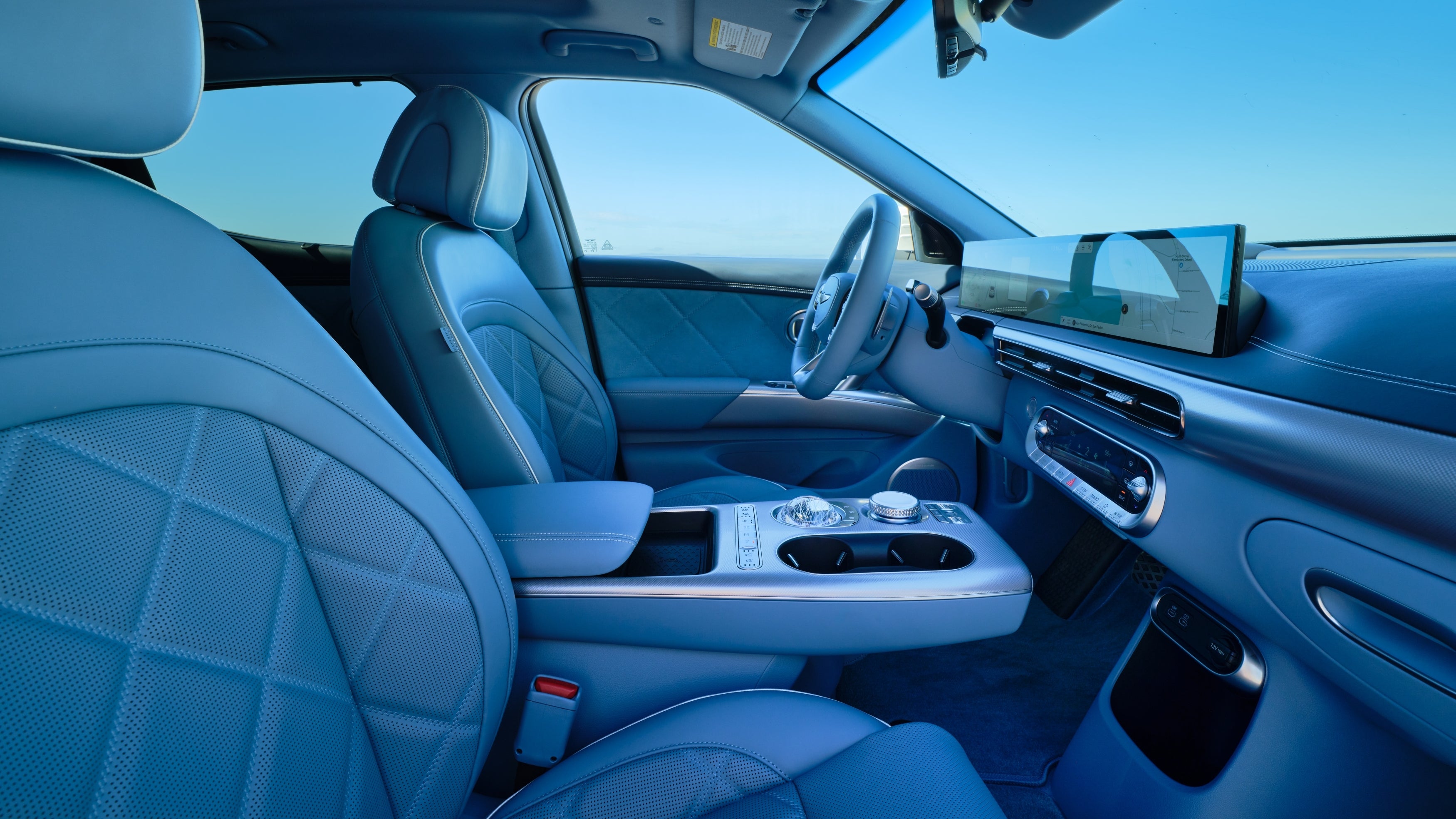 The beautiful aqua green interior of the new GV60 is shown from the passenger seat looking sideways at the driver's seat, front dash and console.
