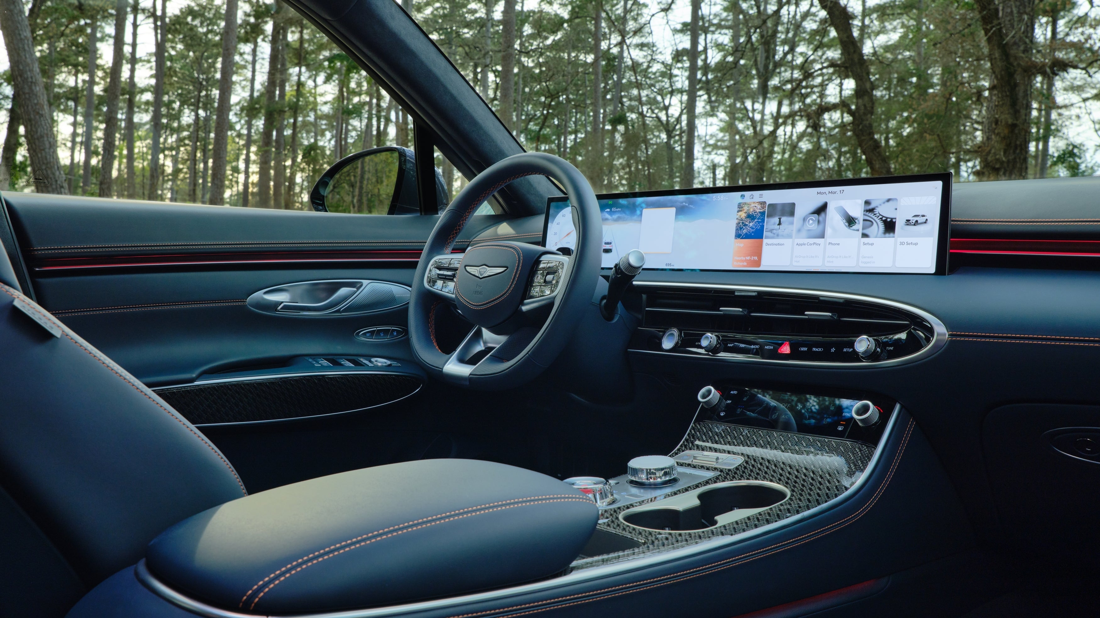 The steering wheel and driver's console of the new Genesis GV70 in Phoenix is shown at an angle from the backseat passenger side.