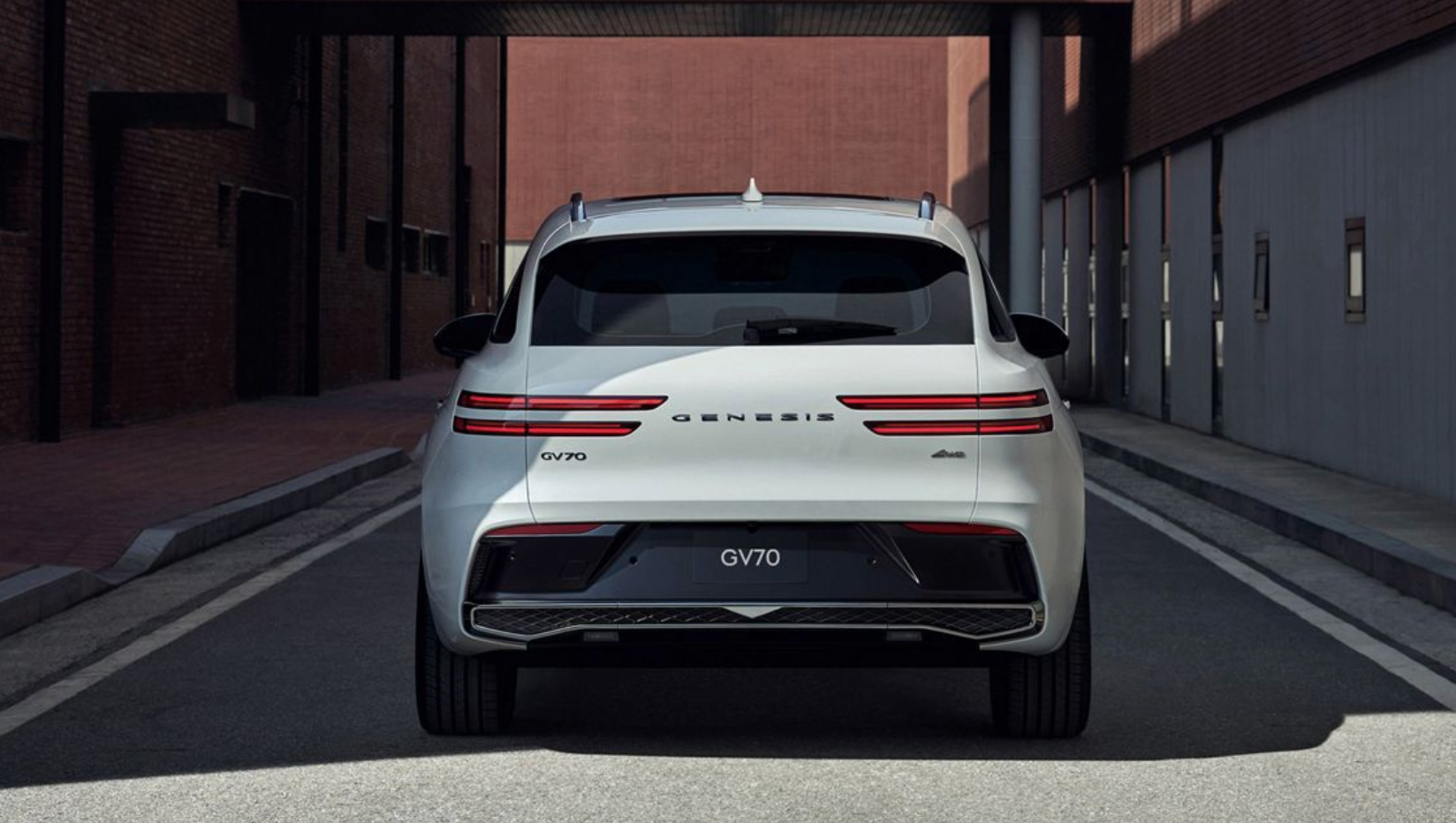 A full rear shot of a white Genesis GV70 SUV, positioned on a city street between two buildings. The vehicle's distinctive thin, horizontal taillights and the 'GENESIS' and 'GV70' badging are clearly visible.
