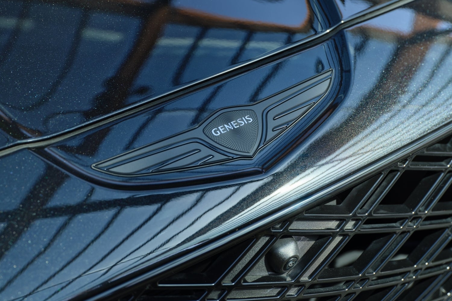 A closeup shot of the Genesis logo in front of the hood on the vik black new Genesis SUV.