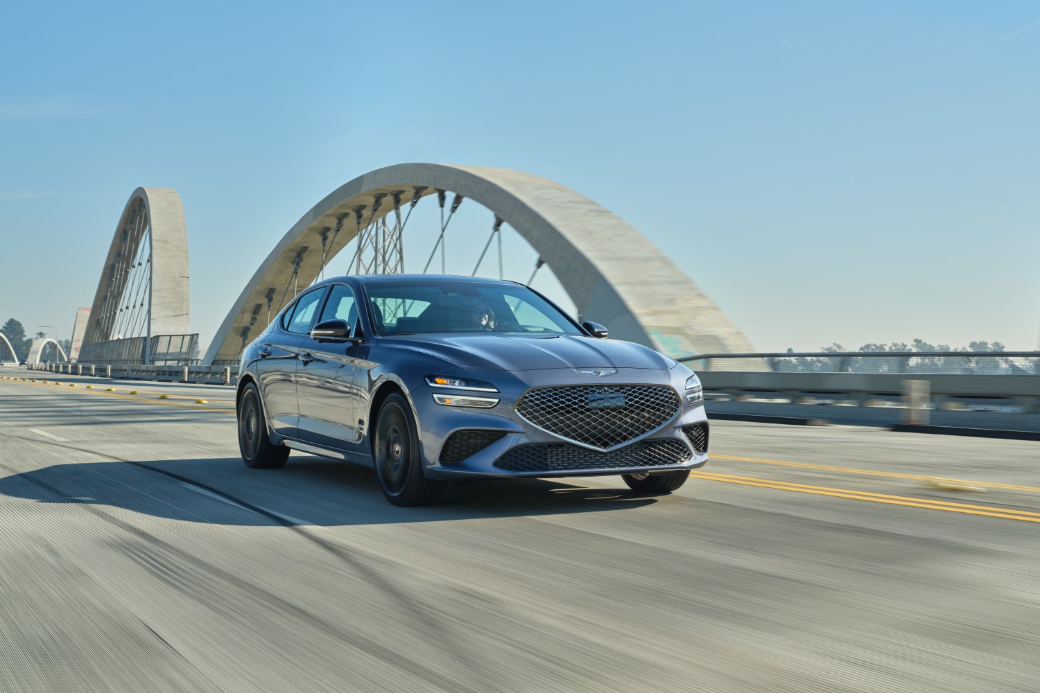 A Prestige Graphite 2026 Genesis G70 in Chandler drives towards the viewer to the right on a city bridge.