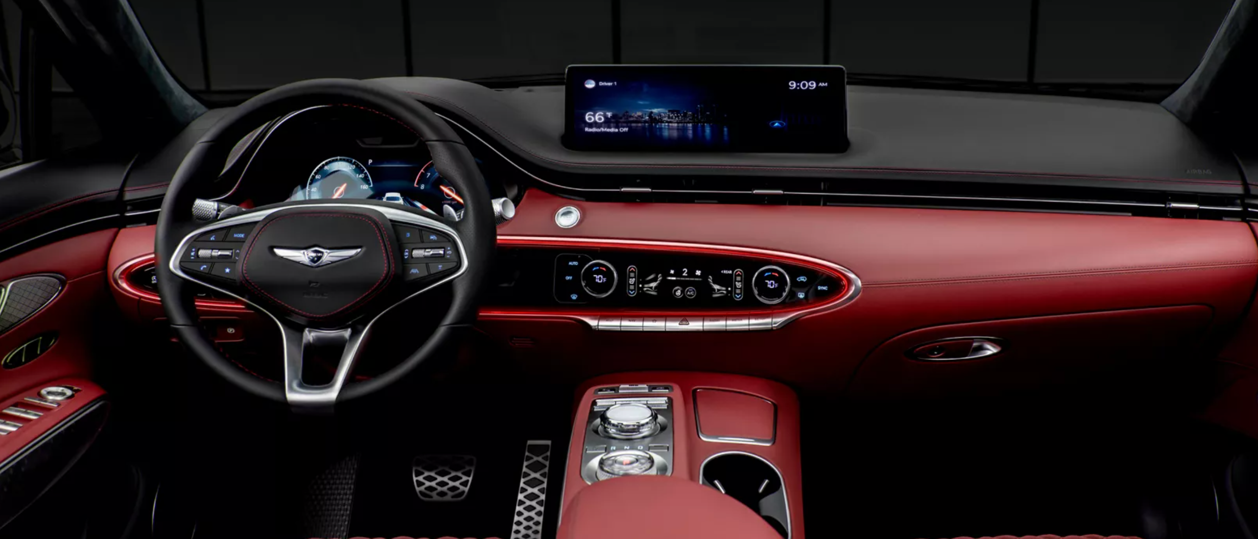 A photo of the interior of a Genesis GV70, showing red leather seats, a black dashboard with a large touchscreen display, and a leather-wrapped steering wheel.